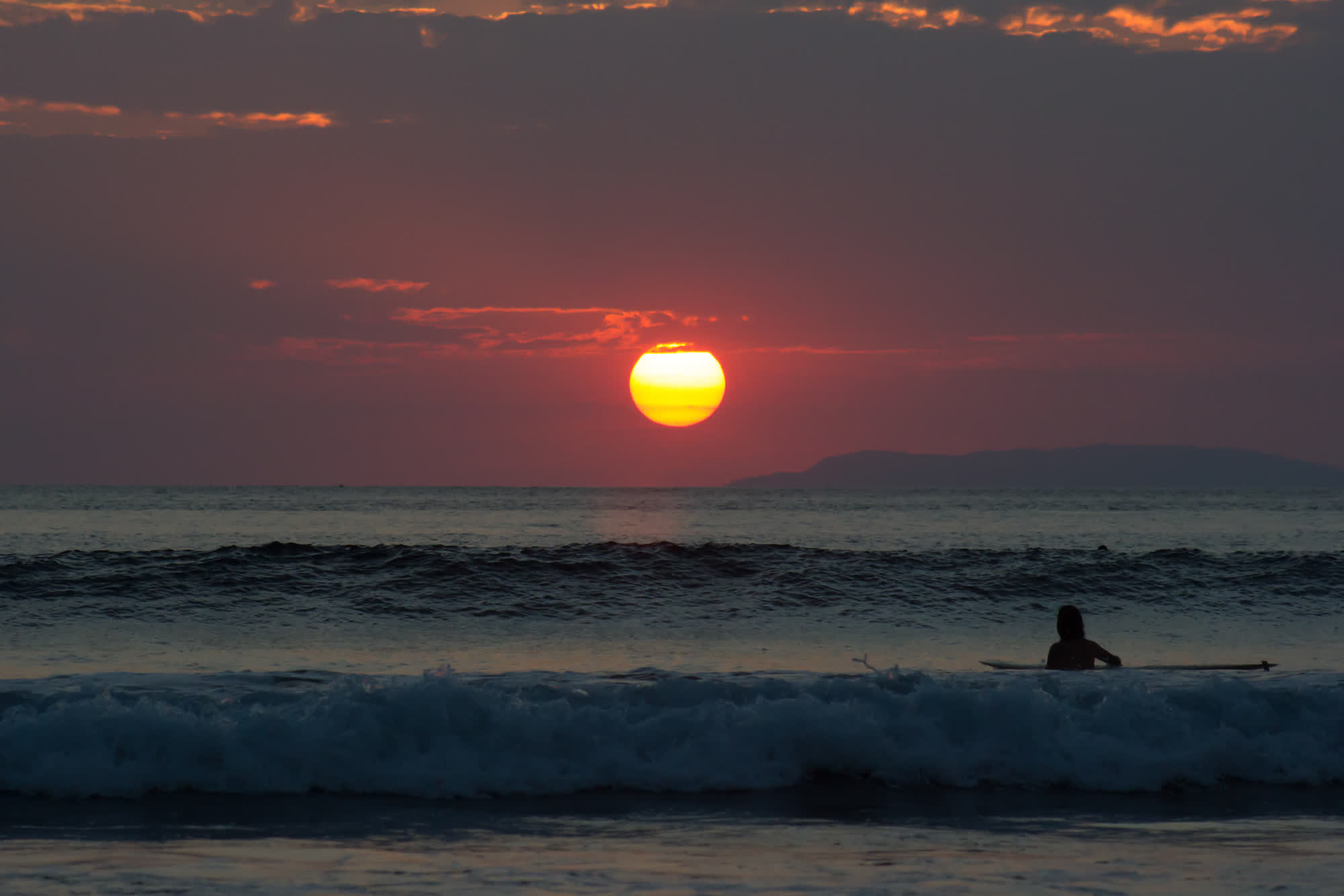 Surfista recortado contra un sol rojo